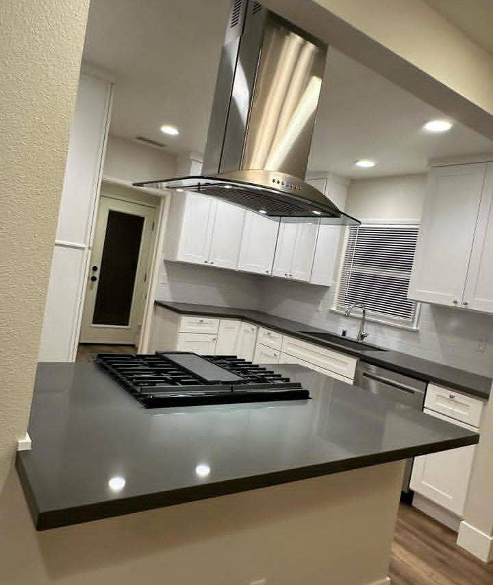 Kitchen island with dark quartz counter and stainless range hood